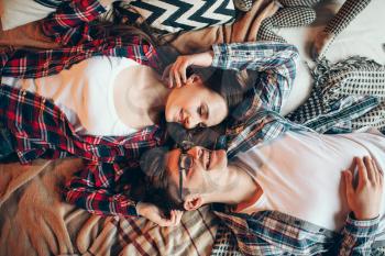 Love couple in clothes embrace on couch, top view. Young wife and husband hugs on the bed in bedroom, snapshot from above 