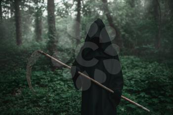 Death in a black hoodie and with a scythe in forest. Horror style, fear, spooky evil