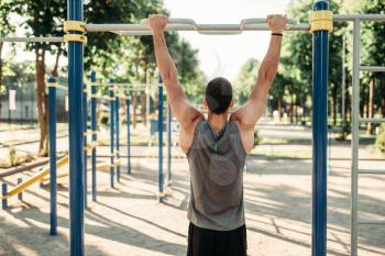 Athletic man doing exercise on horizontal bar on outdoor fitness workout. Strong sportsman on sport training in park