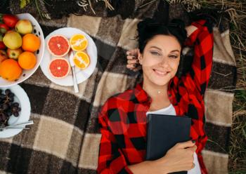 Young woman lies on plaid, top view, picnic in summer field. Romantic junket, happy holiday