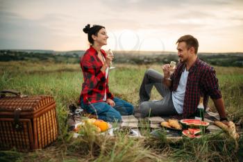 Love couple drinks wine, picnic on the meadow. Romantic junket, man and woman leisure together, happy family weekend