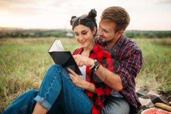 Love couple reads book together, picnic in the field. Romantic junket, man and woman on outdoor dinner,  happy family weekend