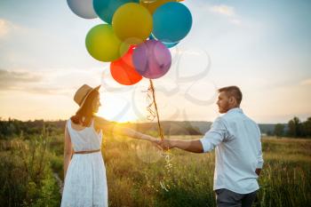 Happy couple holds bunch of balloons and kissing in wheat field. Pretty couple leisure on summer meadow