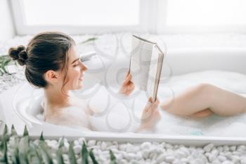 Woman lying in bath with foam and reads magazine, top view. Luxury bathroom with palm branch decor