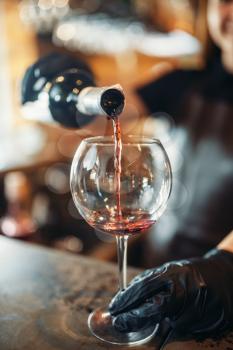 Female barman hands in gloves pours red wine into a glass. Woman bartender working at the bar counter in pub. Barkeeper occupation
