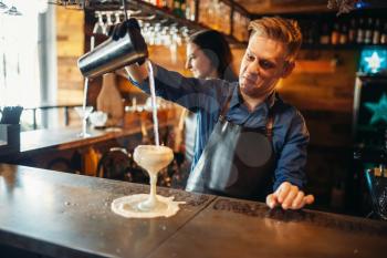 Male barman pouring the drink from the shaker at the bar counter. Alcoholic coctail preparation. Barkeeper occupation, bartending