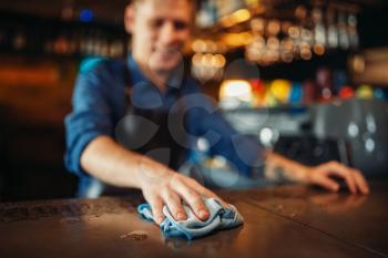 Male barman in apron cleans bar counter. Barkeeper occupation, bartender puts things in order