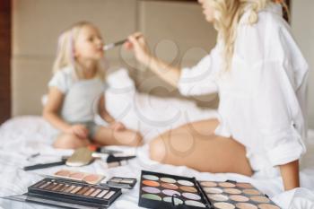Funny mother and child plays with makeup on the bed at home. Parent feeling, togetherness, happy times