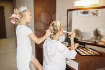 Child makes a funny makeup to her mother against a mirror in bedroom at home. Parent feeling, togetherness, happy times