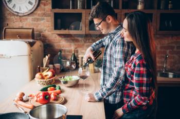 Husband pours wine in a glass, family cooking romantic dinner together.  Couple prepares romantic dinner together. Vegetable salad cooking on the kitchen. Fresh diet food preparation