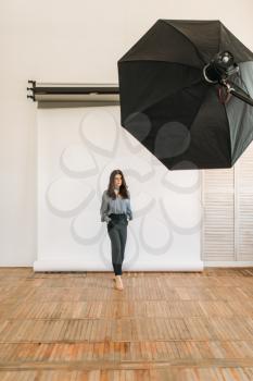 Beautiful model poses in photo studio, white background, lighting equipment. Attractive woman on studio shot