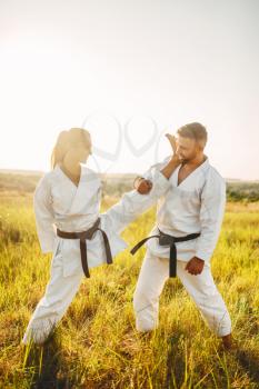 Female karate doing stretching exercise on training with male instructor. Martial art workout outdoor, technique practice, self defense