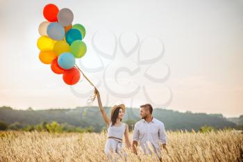 Love couple with colorful air balloons in a rye field. Pretty woman on summer meadow