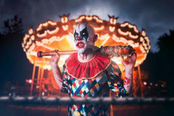 Crazy bloody clown with baseball bat in the amusement park. Man with makeup in halloween costume, scary killer