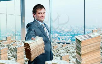 Young businessman holding out a wad of money in office. Loan, investment or credit concept. Businessperson among the pile of bills