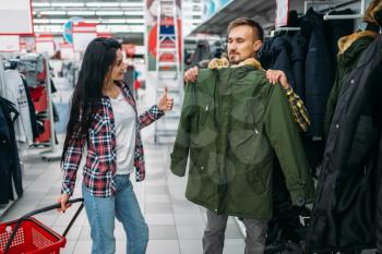 Young couple choosing warm clothes in supermarket. Male and female customers on family shopping. Man and woman purchasing goods for the house