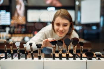 Female customer choosing brushes in the makeup shop. Cosmetics choosing in beauty store, make-up