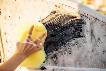 Female person hand with sponge scrubbing vehicle with foam, car wash. Young woman on self-service automobile washing. Outdoor carwash at summer day 