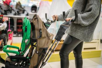 Pregnant woman poses with strollers in childrens goods store. Future mother choosing pushchair for her child