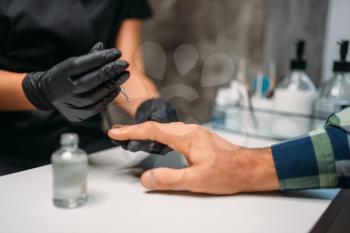 Beautician in black gloves polishing nails to male client, top view, men manicure in salon. Manicurist doing hands care procedure