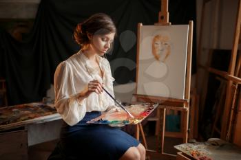 Female painter holds color palette and brush in studio. Creative paintbrush art, artist drawing in class, workshop interior on background
