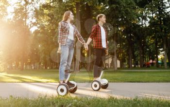 Young couple riding on gyro board in summer park at sunset. Outdoor recreation with electric gyroboard. Transport with balance technology, electrical gyroscope vehicle