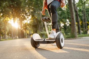 Young male person riding on gyroboard in summer park. Outdoor recreation with electric gyro board. Eco transport with balance technology. Electrical gyroscope vehicle
