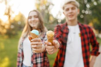 Young couple with ice cream walking in summer park. Boyfriend and girlfriend leisures with ice-cream