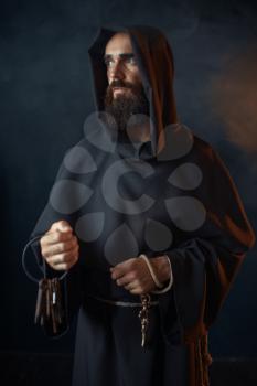 Medieval monk in robe holds a bunch of keys in hands, black background, secret ritual. Mysterious friar in dark cape. Mystery and spirituality
