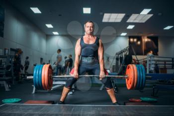 Strong weightlifter doing exercise with barbell, deadlift, gym interior on background. Weightlifting workout in sport or fitness club, bodybuilding
