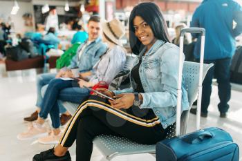 Female black tourist with suitcase waiting for departure in airport. Passengers with baggage looking forward to the flight in air terminal, happy journey, summer travel