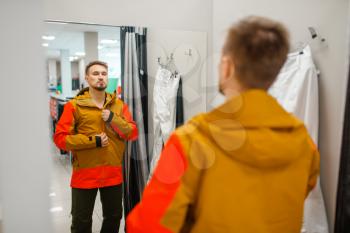 Man trying on a jacket for ski or snowboarding, sports shop. Winter season extreme lifestyle, active leisure, male customer with protect equipment