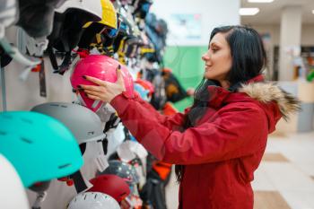 Couple at the showcase choosing helmets for ski or snowboarding, side view, shopping in sports shop. Winter season extreme lifestyle, active leisure store, customers buying protect equipment