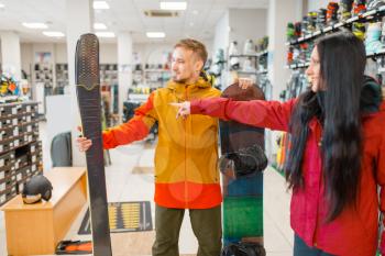 Couple at the showcase choosing downhill ski and snowboard, shopping in sports shop. Winter season extreme lifestyle, active leisure store, customers buying skiing equipment