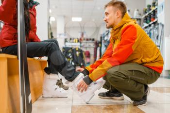 Man helps woman to trying on ski or snowboarding boots, shopping in sports shop. Winter season extreme lifestyle, active leisure store, buyers choosing protect equipment
