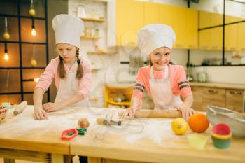 Two little girls chefs with rolling pins, cookies preparation on the kitchen, funny bakers. Kids cooking pastry and having fun, children cooks makes dough and preparing cake