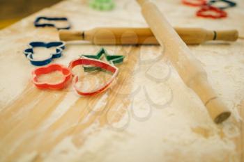 Cookie cutters, rolling pin and flour on wooden table, top view, nobody. Hearts, stars and gingerbread man, pastry templates on the countertop, bakery forms