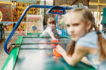 Two little girls plays air hockey in children game center. Excited childs having fun on playground indoors. Kids playing on machine in amusement centre