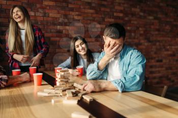 Happy friends plays at the table in cafe. Board game with wooden blocks requiring high concentration, entertainment for funny company