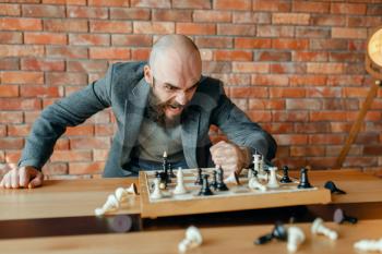 Angry chess player beats his fist on the board with the pieces. Stressed chessplayer in a fit of anger, intellectual tournament indoors. Chessboard on wooden table, strategy game