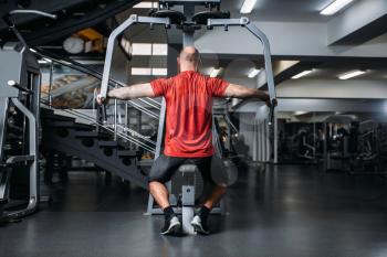Muscular athlete on exercise machine in gym, back view. Sportsman on workout in sport club, healthy lifestyle