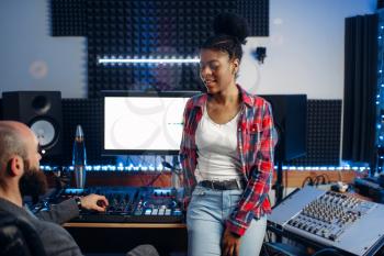 Sound operator and female performer in headphones listens composition in recording studio. Professional audio and music mixing technology