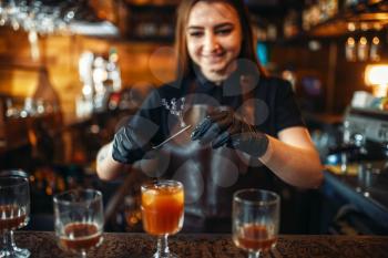 Female bartender holding a glass with coctail over the bar counter. Alcohol drink preparation. Barman working in pub
