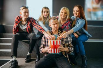 Group of friends poses with popcorn in cinema hall before the showtime. Male and female youth waiting in movie theater, entertainment lifestyle