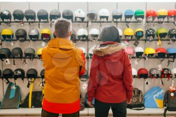 Couple at the showcase choosing helmets for ski or snowboarding, back view, sports shop. Winter season extreme lifestyle, active leisure store, customers with protect equipment