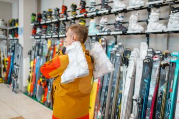 Man carries on his shoulder ski or snowboarding boots in sports shop. Winter season extreme lifestyle, active leisure, male customer choosing protect equipment