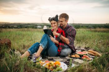 Love couple reads book together, picnic in the field. Romantic junket, man and woman on outdoor dinner, happy family weekend