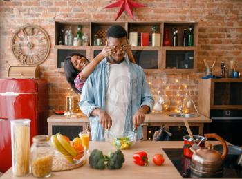 Playful black couple having fun while cooking on the kitchen. African family preparing vegetable salad at home. Healthy vegetarian lifestyle
