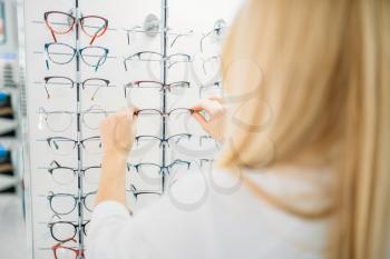 Female optometrist shows glasses in optics store. Selection of eyeglasses with professional optician