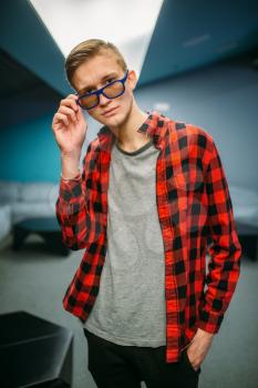 Male teenager in glasses poses in cinema hall before the showtime. Youth in movie theater, entertainment lifestyle, young audience